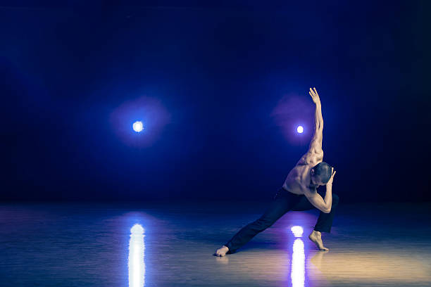 Young and muscular man performing a contemporary dance pose on a stage.
